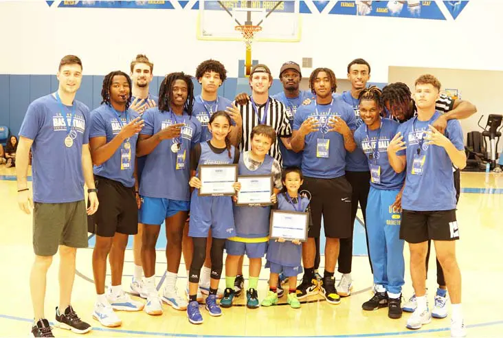 Student-athletes posing with kids on basketball court